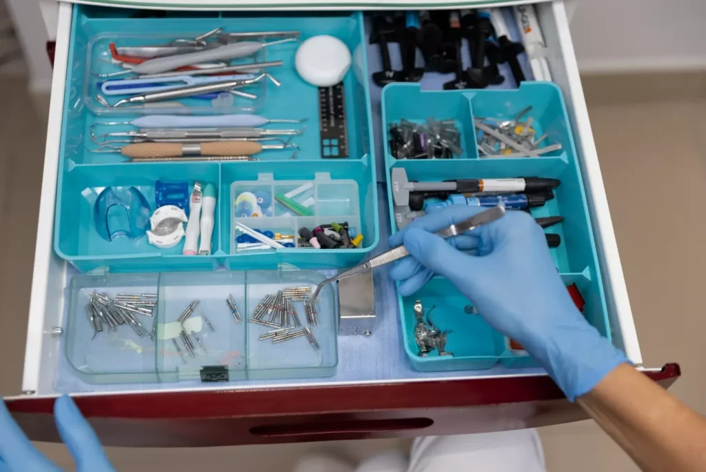 A close-up view of various dental grafting materials arranged on a clean, sterile medical surface. The foreground showcases an array of bone grafting particles, membranes, and collagen sponges used in periodontal and implant procedures. The middle ground features surgical instruments like tweezers and scalpels, highlighting the precision required. The background is a neutral, soft-focus area, creating a sense of clinical focus. The lighting is bright and directional, emphasizing the textural details of the materials. The overall mood is one of medical professionalism, conveying the scientific principles behind dental grafting techniques.