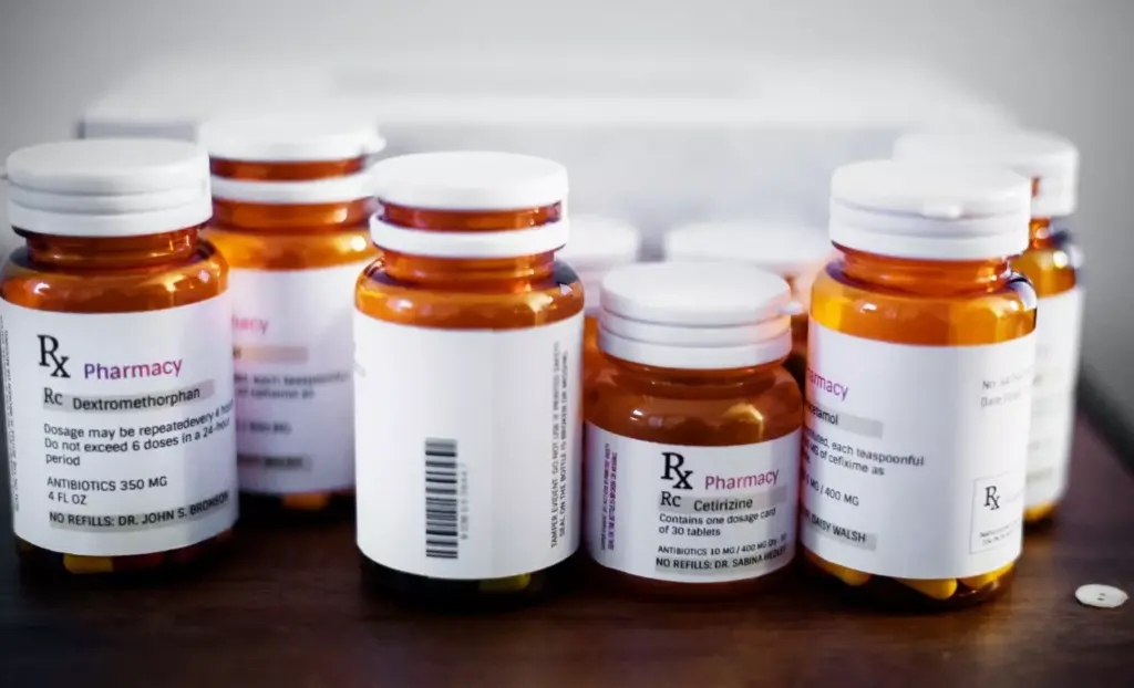 A close-up view of various prescription medication bottles and pill packets arranged on a clean, white surface. The bottles have clear labels displaying the names of common alcohol treatment drugs like disulfiram, naltrexone, and acamprosate. The lighting is soft and even, highlighting the shapes and textures of the pharmaceutical products. The composition emphasizes the therapeutic nature of these medications, conveying a sense of hope and recovery for individuals struggling with alcohol use disorder.