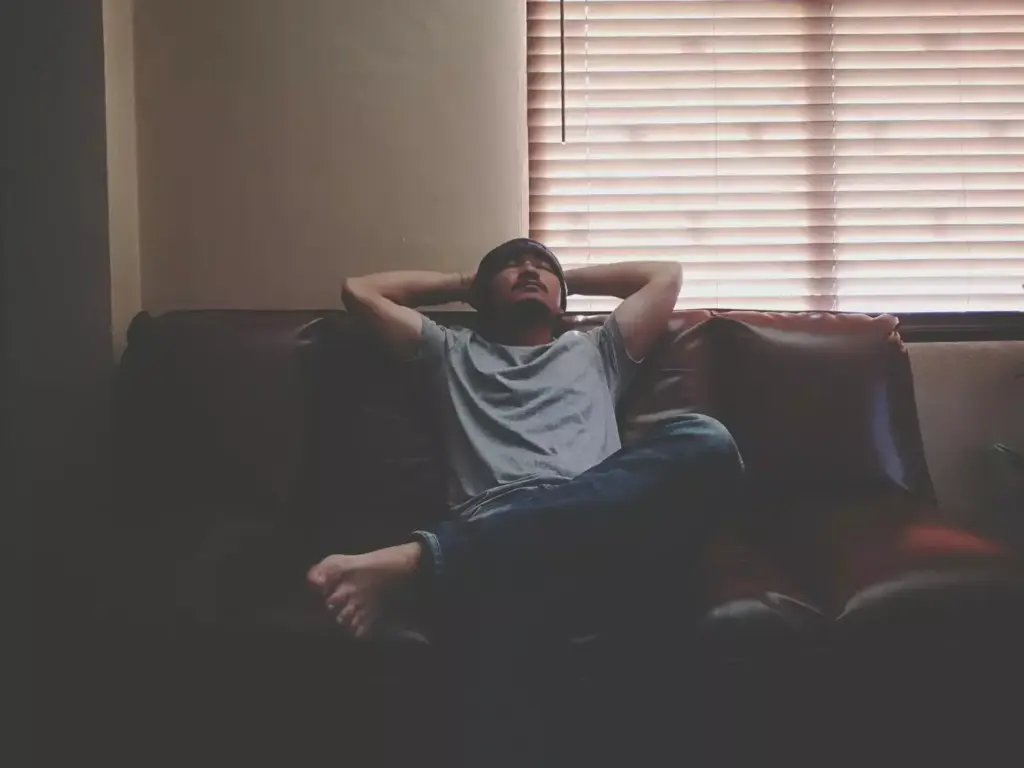 A fatigued individual resting on a couch, their expression weary and their posture slumped. Soft, diffused lighting illuminates the scene, casting a somber, melancholic mood. The middle ground features a messy, cluttered living space, with discarded items and clothing scattered around, reflecting the person's lack of energy and motivation. The background is hazy and out of focus, emphasizing the subject's detachment from their surroundings. The composition conveys a sense of persistent, debilitating tiredness, a common long-term side effect of chemotherapy treatment.