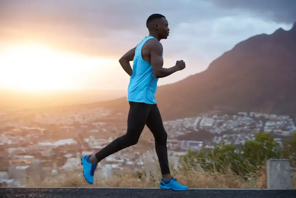 A person in athletic clothing carefully running on a track, their gait slightly uneven due to a recent knee replacement surgery. The runner's expression is one of determination, their eyes focused ahead. The scene is bathed in soft, natural lighting that casts long shadows, conveying a sense of early morning or late afternoon. The background is blurred, placing the focus on the runner's form and the movement of their body. The overall atmosphere is one of perseverance and the gradual return to an active lifestyle after a major medical procedure.