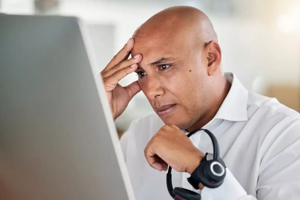 A weary figure, their head bowed, shoulders slumped, sits in a dimly lit room. The lighting casts long shadows, creating a sense of heaviness and fatigue. The background is blurred, with muted tones of gray and blue, emphasizing the central figure's struggle. Soft, diffused light illuminates the person's face, revealing a pensive, exhausted expression. The image conveys the physical and emotional toll of a brain tumor, the burden of the condition weighing heavily on the subject.