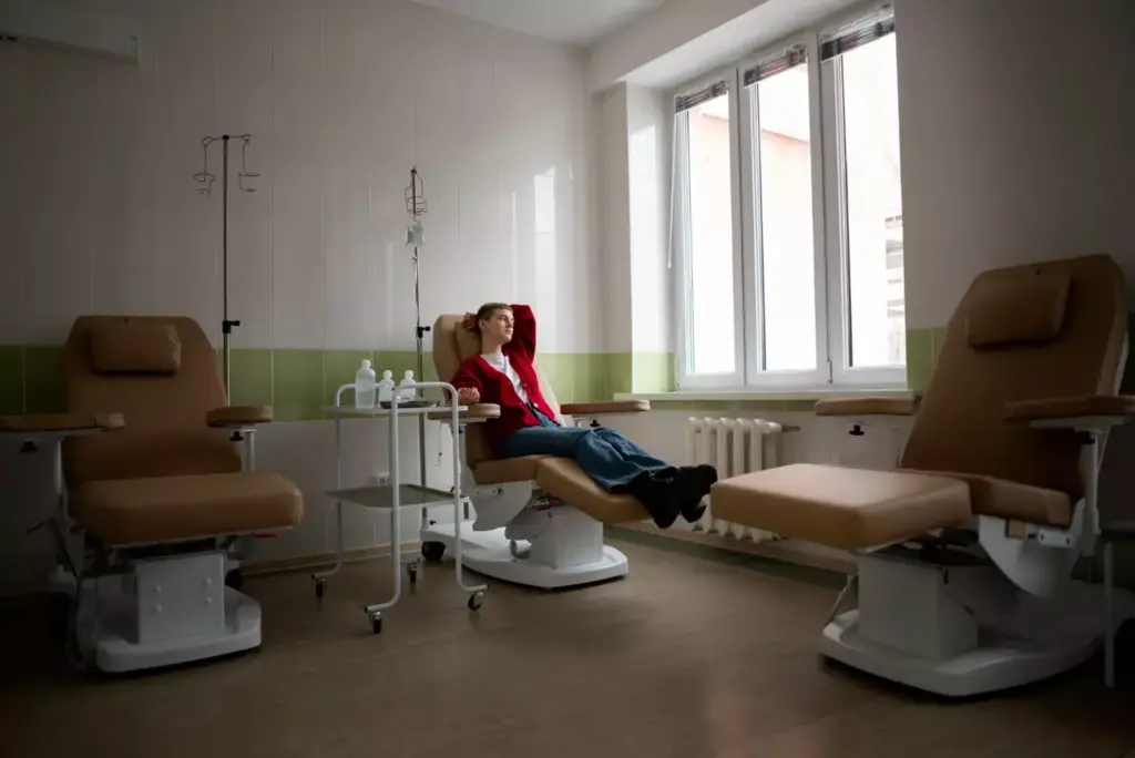 A well-lit, modern oncology infusion therapy suite with large windows overlooking a serene garden. In the foreground, a comfortable reclining chair with IV poles and medical equipment. In the middle ground, a nurse carefully administering chemotherapy medication through an intravenous line. The atmosphere is calm and reassuring, with soft lighting and neutral tones creating a peaceful, therapeutic environment. The angle is slightly elevated, providing a comprehensive view of the treatment process. The image conveys the care and professionalism of oncology infusion therapy.