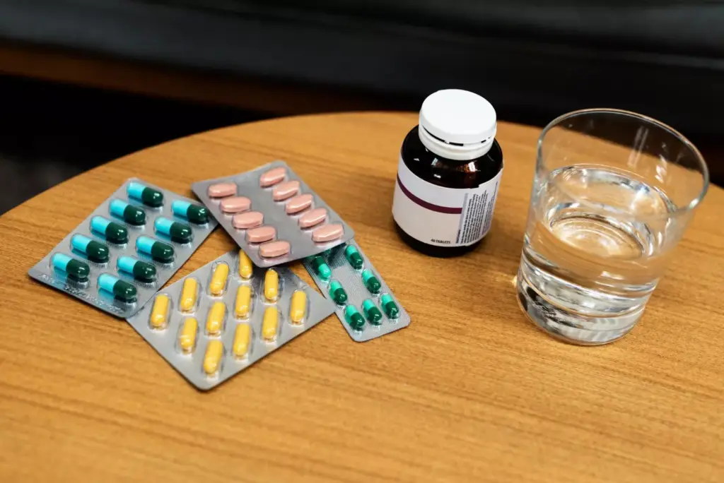 An assortment of prescription medications and supplements for alcohol rehab, arranged neatly on a clean, modern desktop surface. Bottles, blister packs, and pill containers in the foreground, with a neutral, calming background that evokes a professional medical setting. Warm, soft lighting from above casts a comforting glow, highlighting the various colors and shapes of the rehab drugs. The image conveys a sense of care, treatment, and the comprehensive approach to alcohol recovery through pharmaceutical interventions.