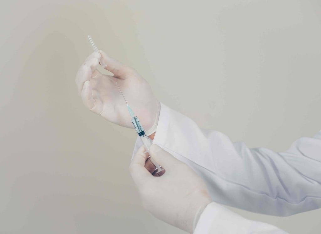 doctor's gloved hands hold a medical syringe filled with bone marrow fluid.
